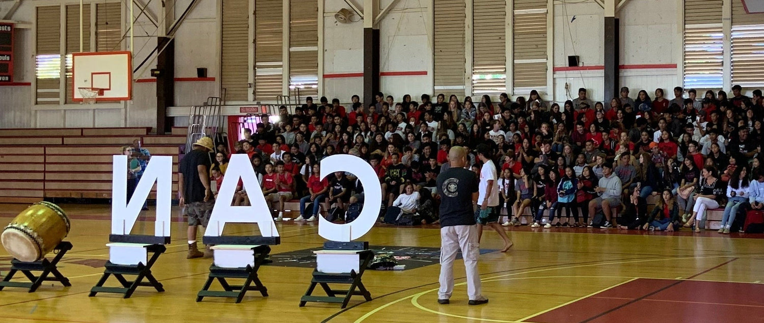 Large indoor gymnasium with a basketball court, large letters spelling 'CANADA', and people in the stands.